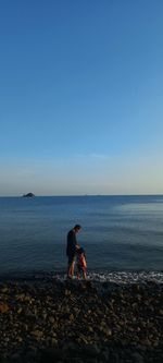 Rear view of father and his daughter at beach against sky