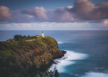 Lighthouse on rock by sea against sky