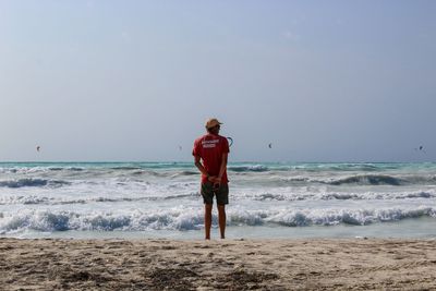 Rear view of man standing on beach against clear sky