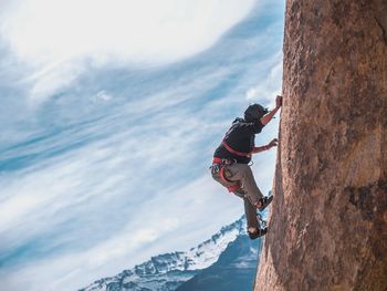 Man climbing cliff against sky