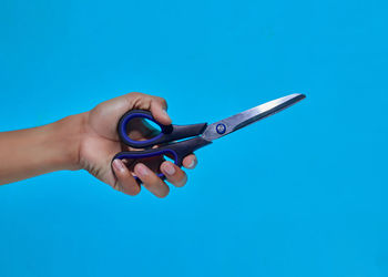 Close-up of hand holding eyeglasses against blue background