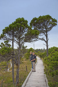 Father and son standing on footpath amidst trees against clear sky