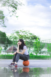 Full length of young woman sitting at basketball court