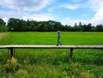 Side view of man on boardwalk over field against sky