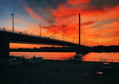 Silhouette bridge over river against orange sky