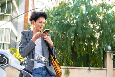 Woman with short haircut sits on bike and uses her phone