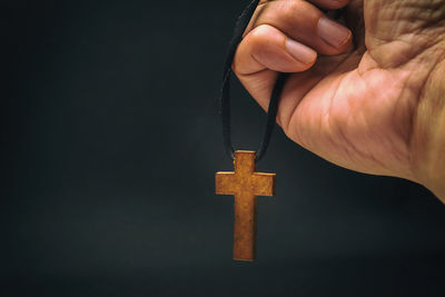 Midsection of person holding cross against black background
