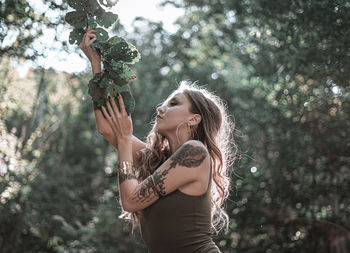 Portrait of woman with arms raised standing against trees