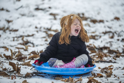 Girl shouting while sitting on sled at snow field