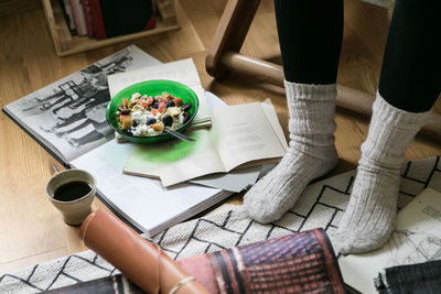 Low section of businesswoman wearing socks while standing by breakfast and books at home office