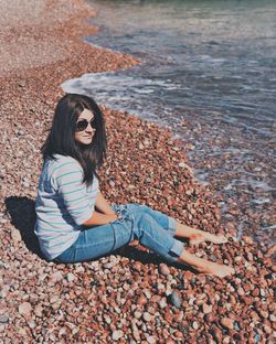 Portrait of smiling woman sitting on pebbles at beach