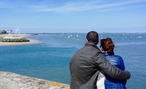 Rear view of couple overlooking calm blue sea