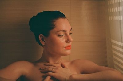 Close-up of thoughtful topless young woman looking away against wall at home