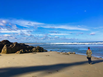 Rear view of woman standing on sand at beach against sky