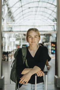 Portrait of smiling woman with luggage standing at station