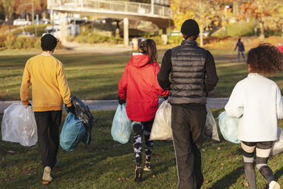 Rear view of young environmentalists walking with plastic waste in park