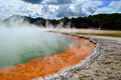 Scenic view of hot spring against cloudy sky during sunny day