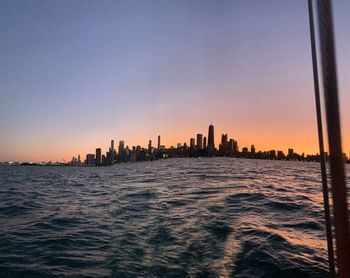 Sea by buildings against sky during sunset