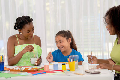 African american teacher helping to clean paintbrush to latin student girl in art class