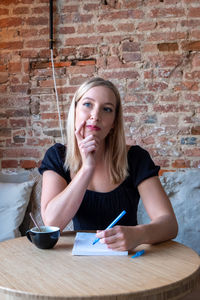 Young woman using pen and paper to write down ideas while sitting at a table in a coffee bar