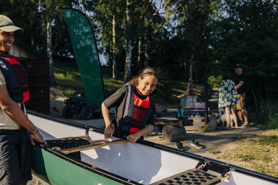 Portrait of smiling girl helping counselor while carrying kayak at summer camp