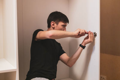 A young man is tightening the screws on the fittings inside the wardrobe.