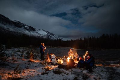 People sitting by campfire at lakeshore during winter