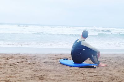 Man sitting on beach against sky