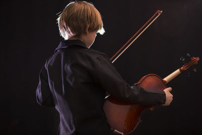 Boy playing violin against black background