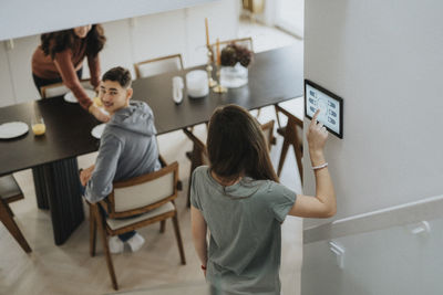 Girl using digital tablet mounted on wall and talking with brother at home