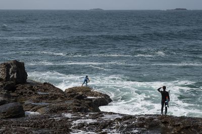 People standing on rocks by sea