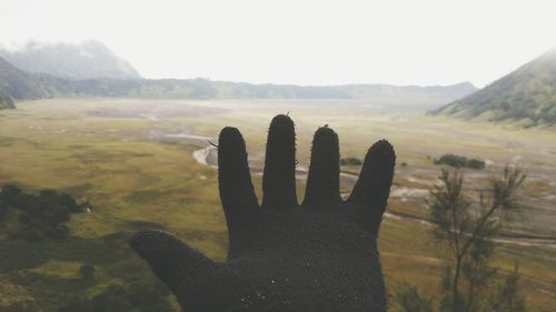 Close-up of hand wearing glove against landscape