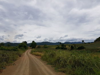 Empty road amidst field against sky