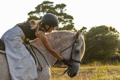 Lusitano horse, white mare, female rider, outdoors on pasture.