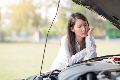 Sad young woman leaning on engine of car