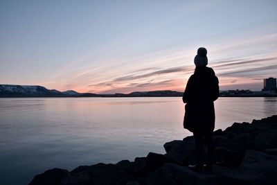 Silhouette woman standing on rock by sea against sky during sunset