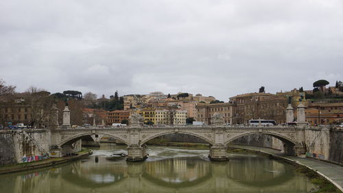 Bridge over river by buildings against sky in city