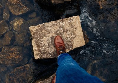 Low section of person wearing shoe while standing on rock amidst water