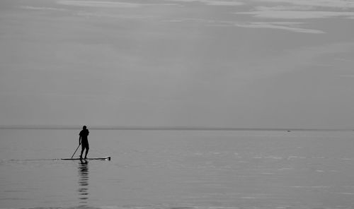 Man paddleboarding at sea against sky