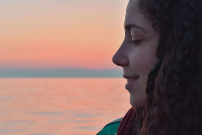 Close-up portrait of woman looking at sea against sky during sunset