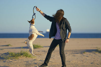 Woman playing with dog at beach against sky