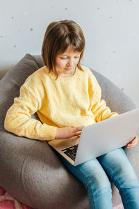 A girl sits in her room with a laptop on her lap and watches lessons or training courses. 