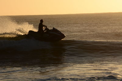 Silhouette man sitting in sea against sky during sunset