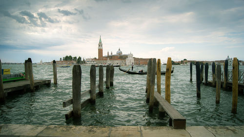 Wooden posts in sea against cloudy sky