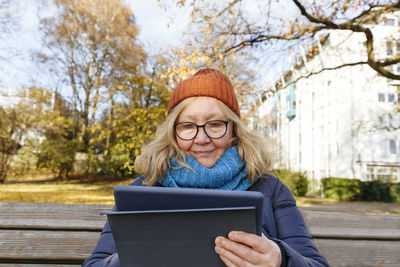 Senior woman using tablet pc sitting on bench in park