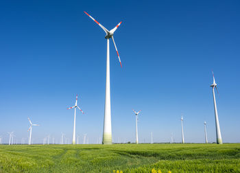 Windmills on field against clear blue sky