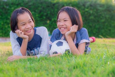 Happy sisters lying down on grassy land with soccer ball