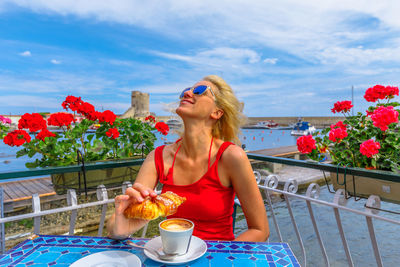 Woman wearing sunglasses and red flowers on table against sky