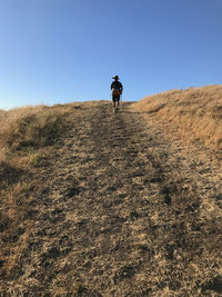 Rear view of man walking on mountain against clear sky