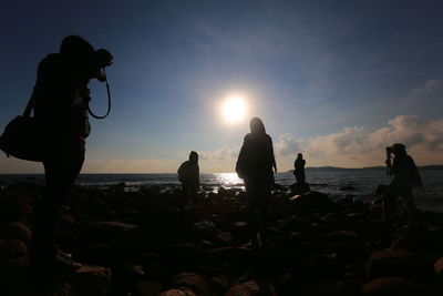 Silhouette people on beach against sky during sunset